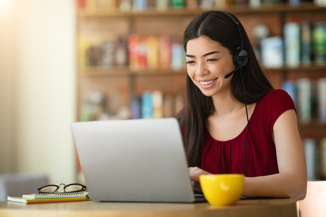Online Tutoring. Asian Woman Tutor With Headset Working On Laptop In Cafe